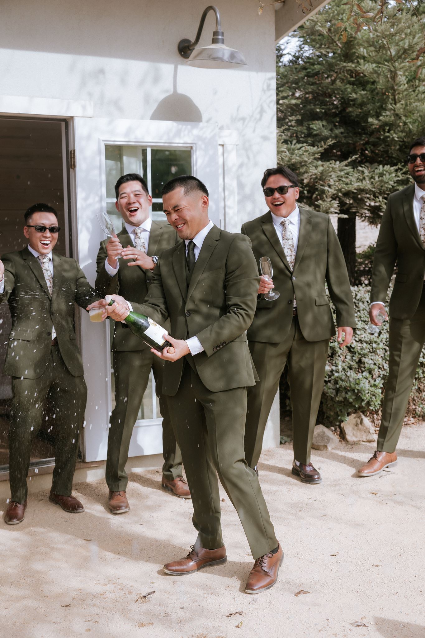 Groom popping a bottle of champagne during getting ready with his groomsmen